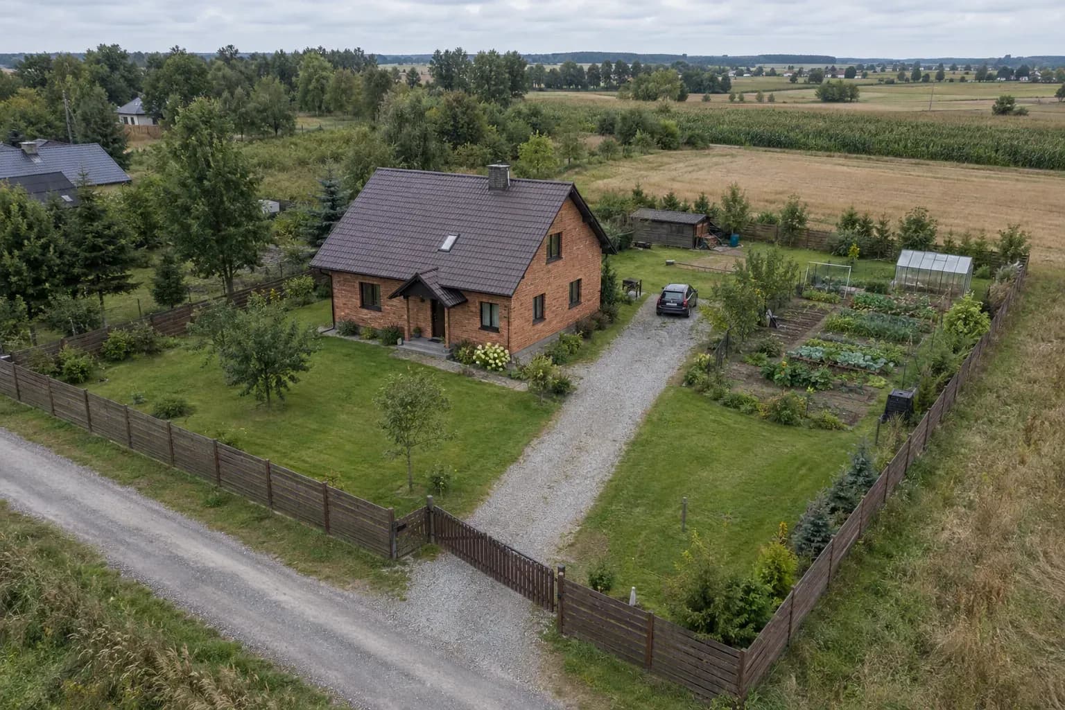 Widok z góry na działkę: dom jednorodzinny, podjazd i ogród warzywny